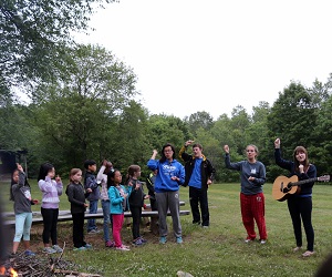 Counsellors lead campers in singing worship songs outside.