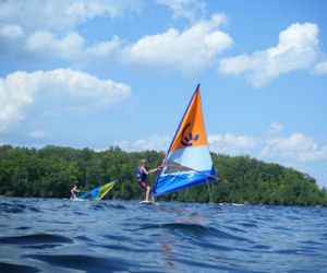 A camper balances on a windsurfer during free swim.